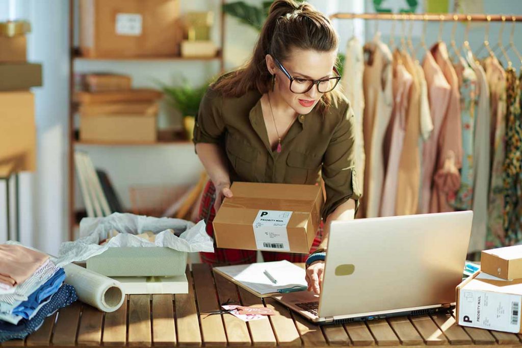 stylish middle aged small business owner woman with parcel using laptop in the office.