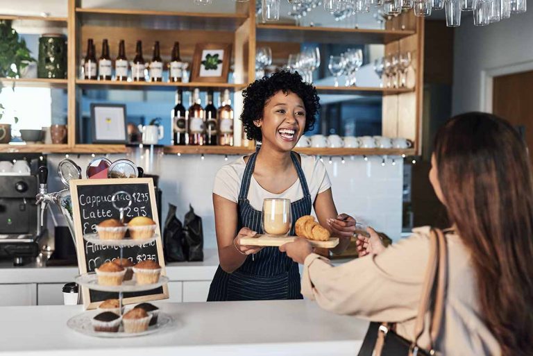 Happy woman, barista and serving customer at cafe for service, payment or order on counter at coffee shop.